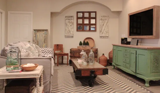 Living room with gray sofa, patterned rug, green vintage-style cabinet under a mounted TV, and rustic decor accents; warm and inviting.
