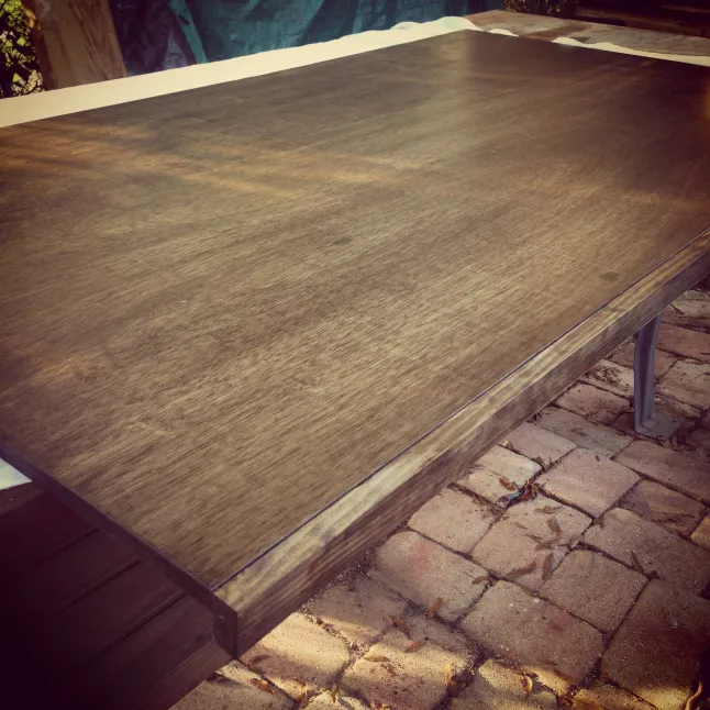 Close-up of a dark stained wooden tabletop outdoors on a brick patio; warm brown tones, quiet calm mood.